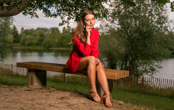 Грустная девушка в красном пальто сидит на лавке