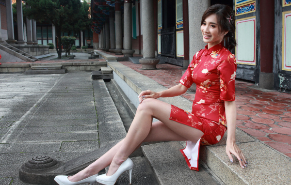 Улыбающаяся девушка азиатка в красном платье сидит на ступеньках