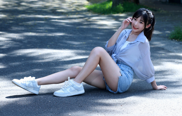 Улыбающаяся девушка азиатка в кедах сидит на дороге