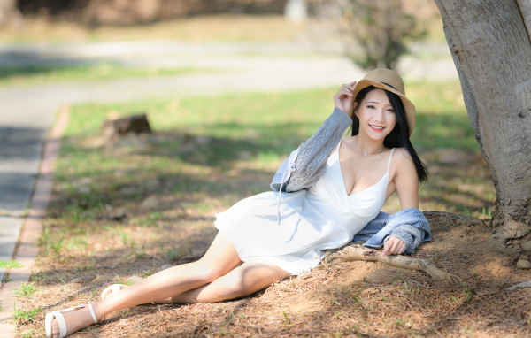 Улыбающаяся азиатка в белом платье лежит под деревом