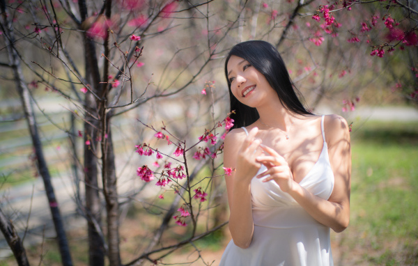 Улыбающаяся девушка в белом платье у дерева с цветами