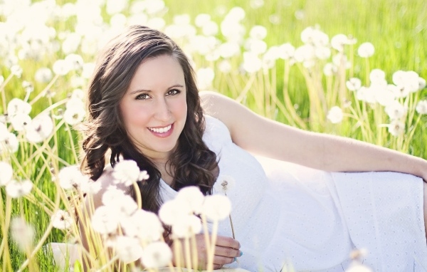 Улыбающаяся девушка лежит на поле с одуванчиками