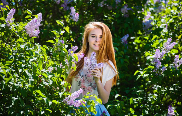 Улыбающаяся девушка стоит у куста сирени