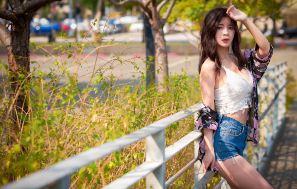 Молодая азиатка в синих шортах стоит у забора