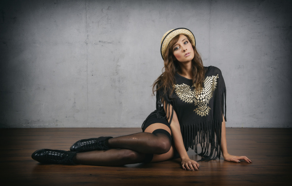 Молодая девушка сидит на полу на фоне серой стены