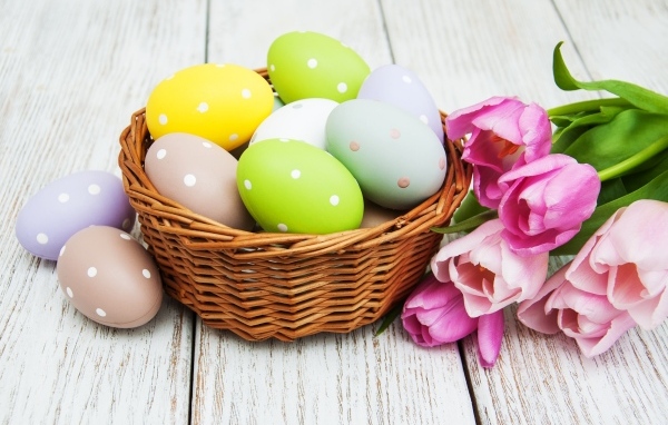 Корзина разноцветных яиц с тюльпанами на столе на Пасху
