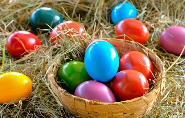 Разноцветные пасхальные яйца в корзине на сене