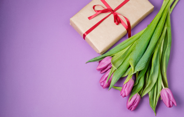 Подарок и букет красивых тюльпанов на сиреневом фоне