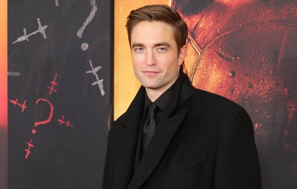 Популярный актер Роберт Паттинсон в костюме стоит у стены