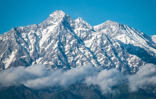 Высокие заснеженные горы в тумане под голубым небом