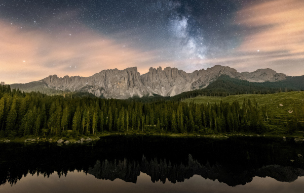 Млечный путь над горами и лесом отражающимися в воде