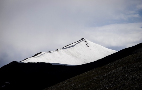 Заснеженная вершина горы под грозовым небом