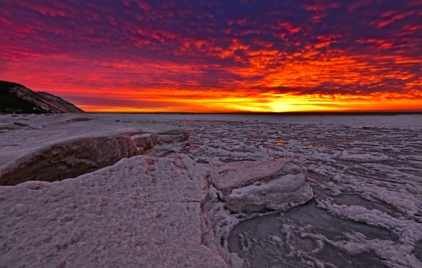 Красный закат солнца покрывает заледеневшее озеро 