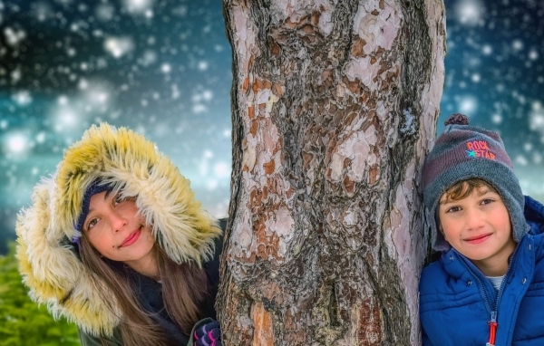 Мальчик и девочка стоят у дерева зимой