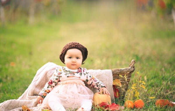 Милая маленькая девочка в шапке сидит на траве 