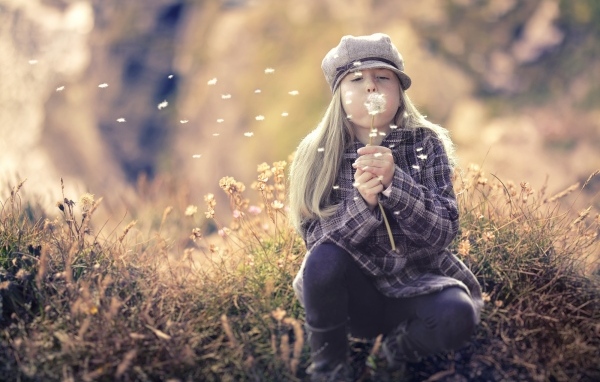 Девочка в кепке сдувает одуванчик