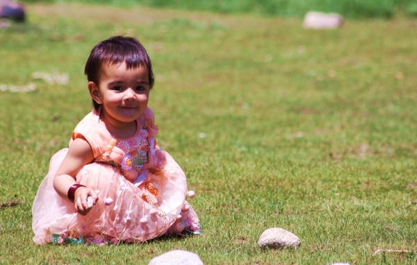Девочка в розовом платье играет на зеленой траве