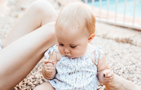 Маленькая светловолосая девочка сидит на песке