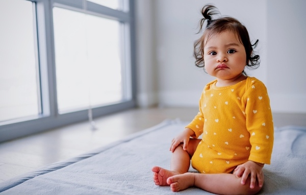 Маленькая смешная девочка сидит у окна