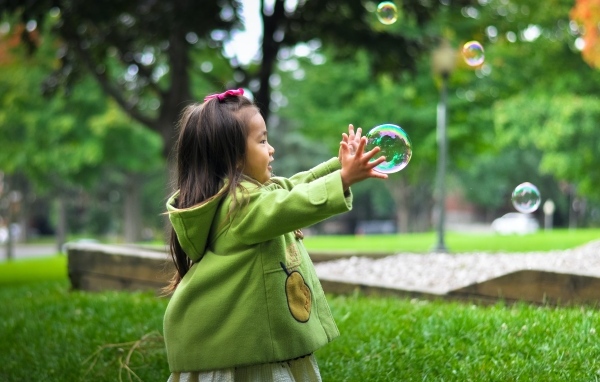 Маленькая девочка ловит мыльные пузыри