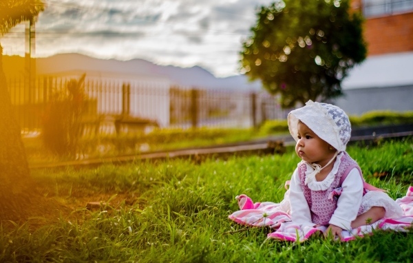 Маленькая девочка в розовом платье сидит на траве