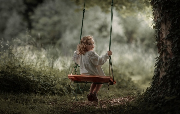 Маленькая девочка на качели в саду