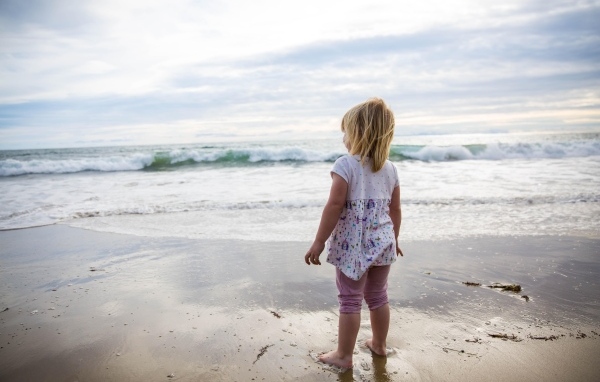 Маленькая девочка стоит на берегу моря