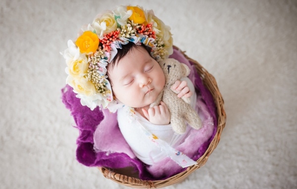 Новорожденная девочка с венком на голове спит в корзине