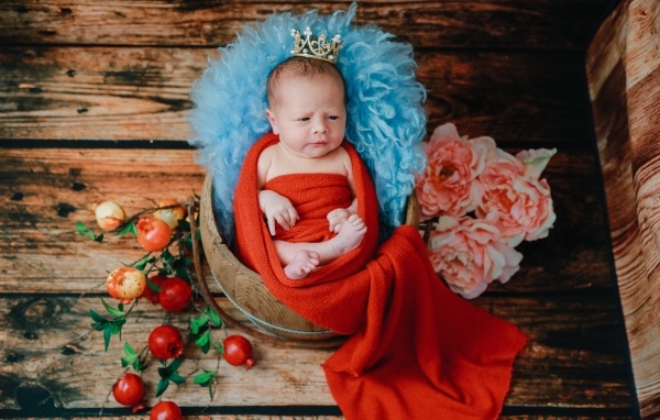 Новорожденный ребенок в красном покрывале с короной на голове 