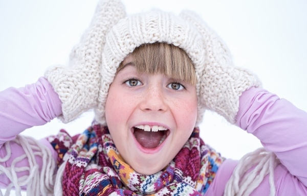 Довольная девочка в вязаной шапке и варежках