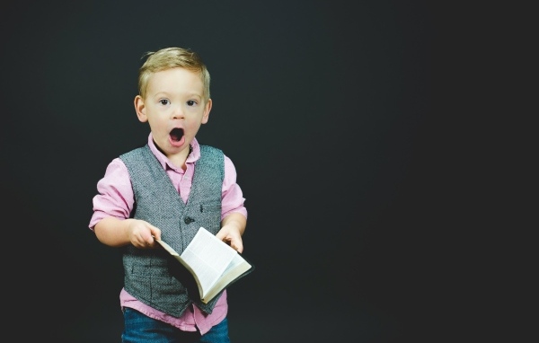 Удивленный мальчик с книгой в руках на черном фоне