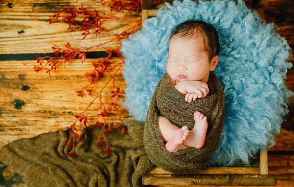 Крошечный новорожденный ребенок на голубой меховой подушке