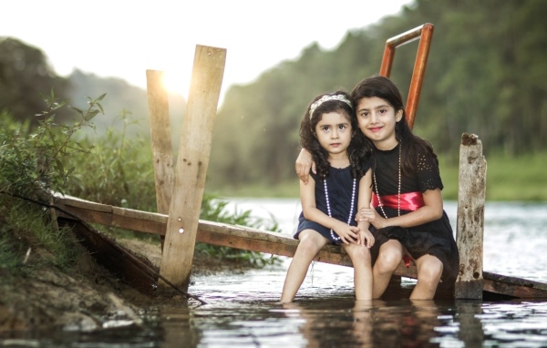 Две девочки сидят на мосту у реки