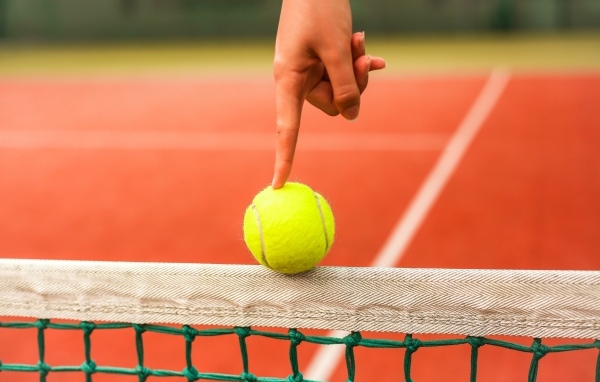 Палец держит желтый теннисный мяч