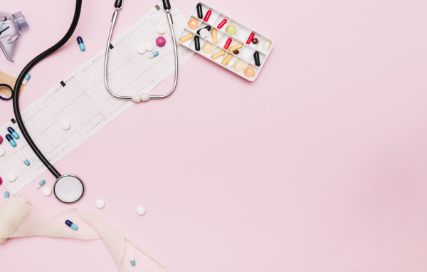Стетоскоп и лекарства на кардиограмме на розовом фоне