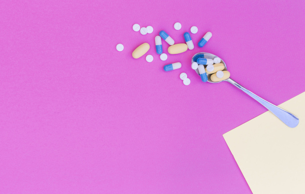 Таблетки с ложкой на розовом фоне