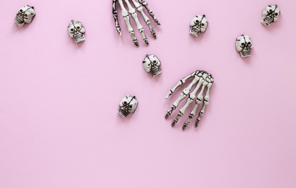 Кисти рук скелета и черепа на розовом фоне