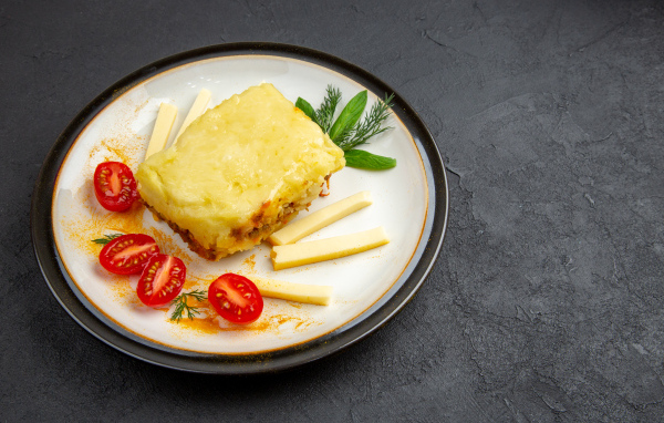 Кусок картофельной запеканки на тарелке с помидорами