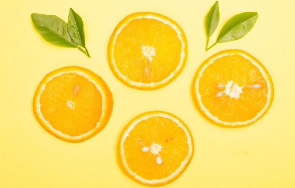 Нарезанный апельсин с зелеными листьями на желтом фоне