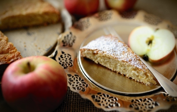 Кусок пирога с сахарной пудрой на столе с яблоками