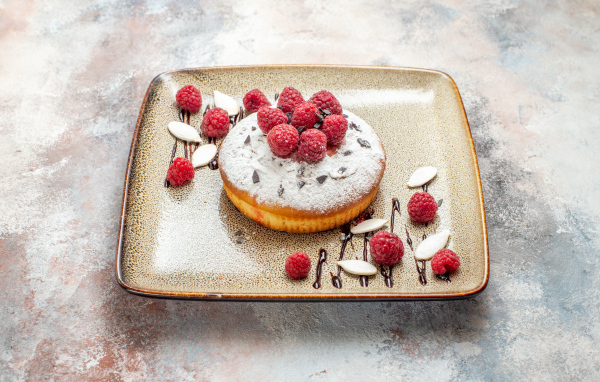 Пирожное с сахарной пудрой и малиной на тарелке