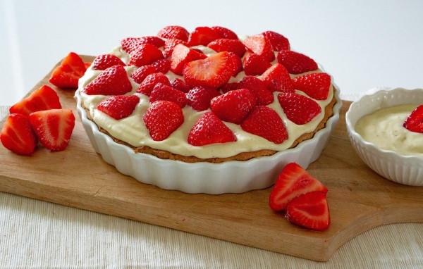 Большой пирог с кремом и ягодами спелой клубники на столе