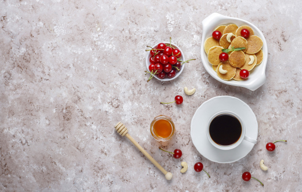 Оладьи на столе с вишней, кофе и медом