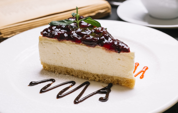 Кусок чизкейка с джемом на белой тарелке
