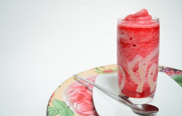 Стакан красного ягодного смузи на столе с чайной ложкой