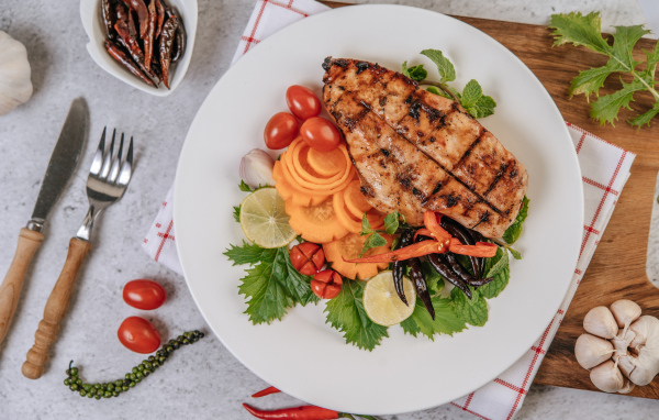 Кусок жареной курицы на большой белой тарелке с овощами