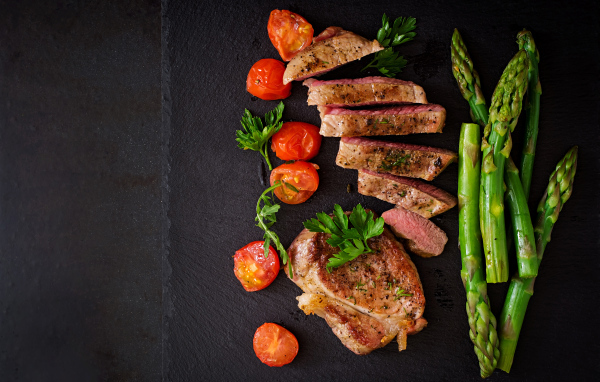 Нарезанный кусок мяса с помидорами и зеленой спаржей