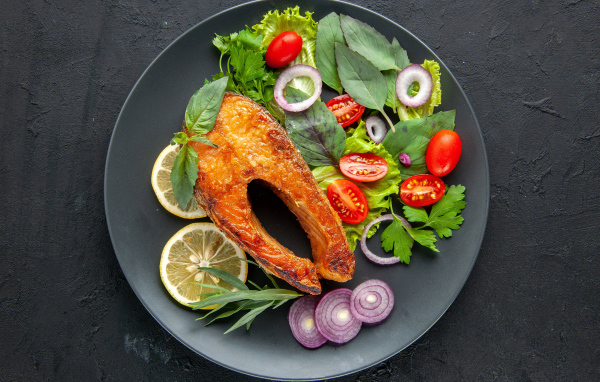 Жареная рыба на тарелке с зеленью,  лимоном и помидорами