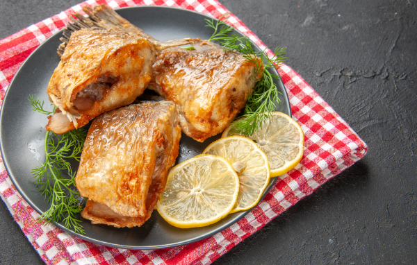 Куски жареной рыбы на тарелке с кусочками лимона и укропом