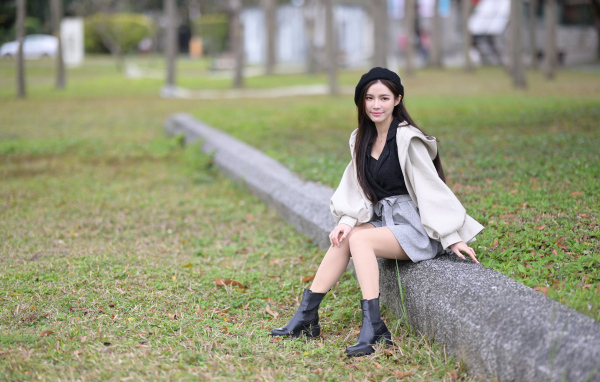 Девушка в пальто сидит на земле в парке